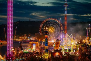 Blick auf den Festplatz bei Nacht mit den Lichtern der vielen Fahrgeschäfte. Dominant das beleuchtete Riesenrad, die Fruchtsäule und das Riesenbier auf dem Festzelt Wasenwirt.