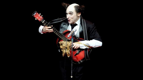Clown vor schwarzem Hintergrund, der Gitarre spielt.