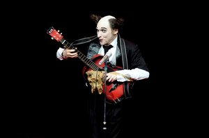 Clown vor schwarzem Hintergrund, der Gitarre spielt.