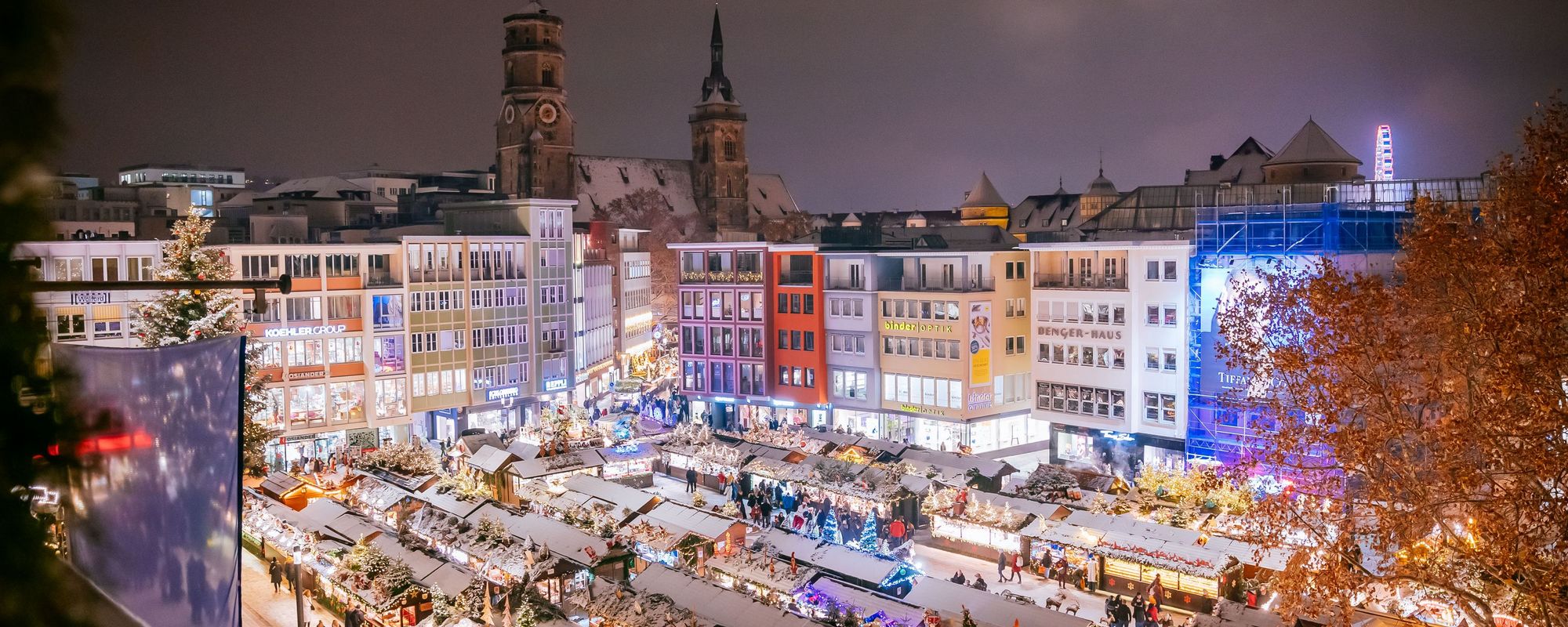 Vogelperspektive auf den Weihnachtsmarkt auf dem Rathausplatz - die Buden sind mit Schnee bedeckt und leuchtenin der Dunkelheit auf dem Platz